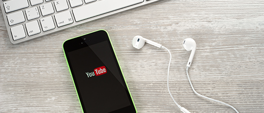 Symbolbild: Handy, auf dem Display ist das Logo von Youtube zu sehen. Im Hintergrund ist eine Computertastatur