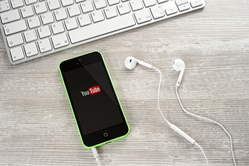 Symbolbild: Handy, auf dem Display ist das Logo von Youtube zu sehen. Im Hintergrund ist eine Computertastatur