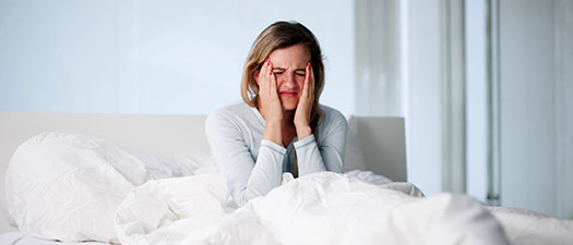 Symbolbild: Eine Frau sitzt aufrecht im Bett und reibt sich das Gesicht.