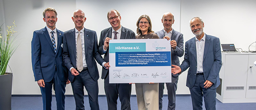 Foto der Gründungsmitglieder der HörHanse, die eine überdimensionale, symbolische Gründungsurkunde in den Händen halten