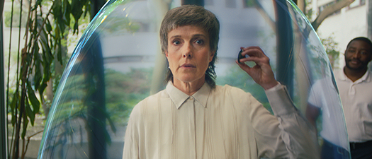 Symbolbild: Foto einer Frau, die in einer großen Seifenblase steht und sich einen Soundprozessor vors Ohr hält