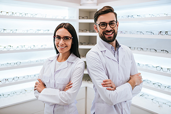 Auf dem Foto sind eine Optikerin und ein Optiker in ihrem Geschäft mit zahlreichen Brillen im Hintergrund zu sehen.